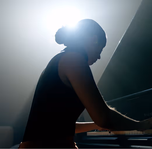 Anna Genov im Halbschatten spielt Klavier, Licht scheint von hinten über den Kopf.