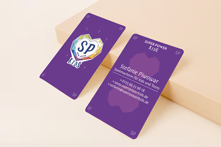 Zwei violette Visitenkarten für Super Power Kids mit einem bunten Herzlogo und Kontaktdaten von Stefanie Piwowar.