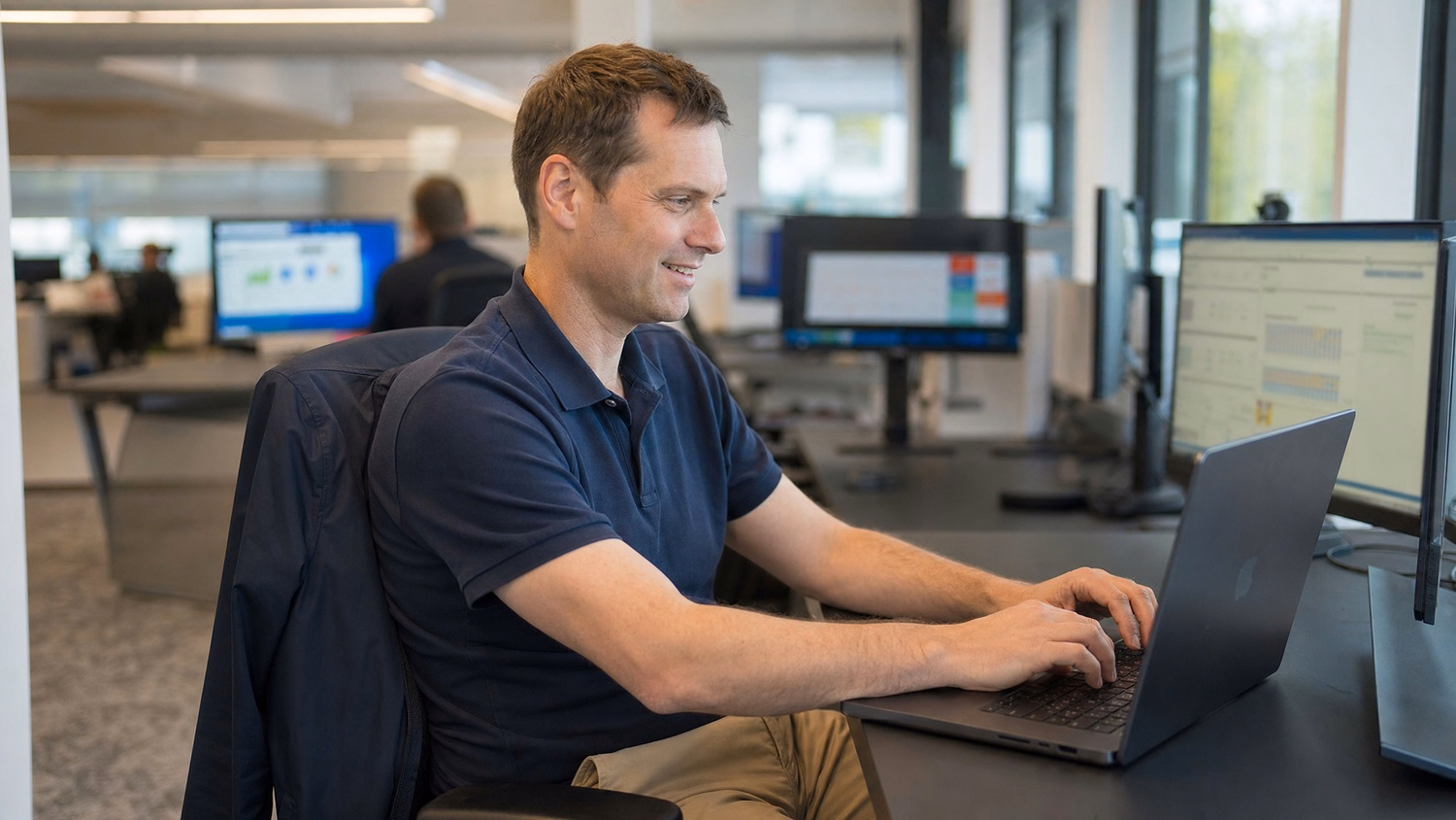 A Caucasian man in his 40s, wearing a navy polo shirt and chinos, is seated at a