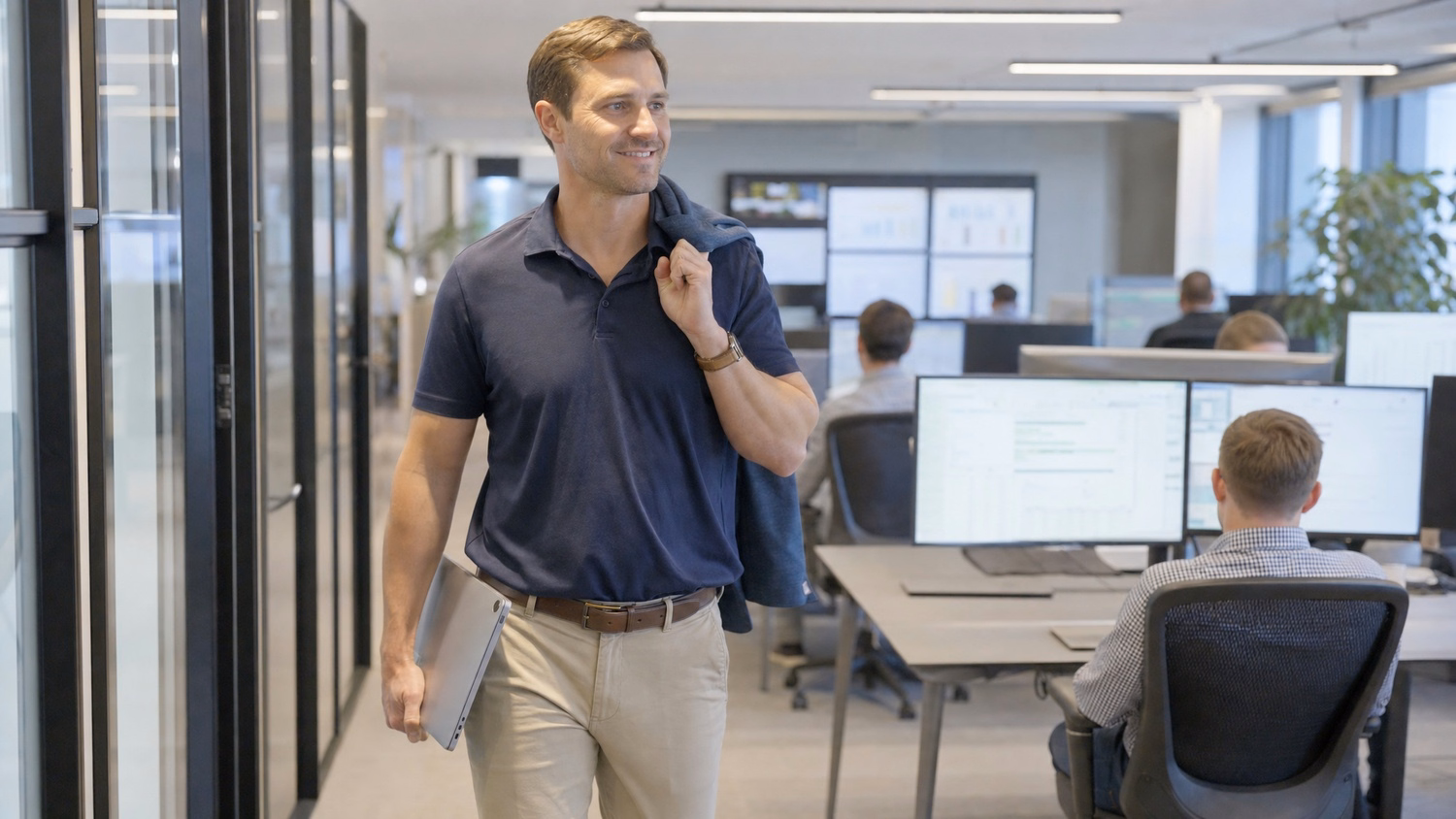 IT technician walks office corridor with laptop, blue jacket