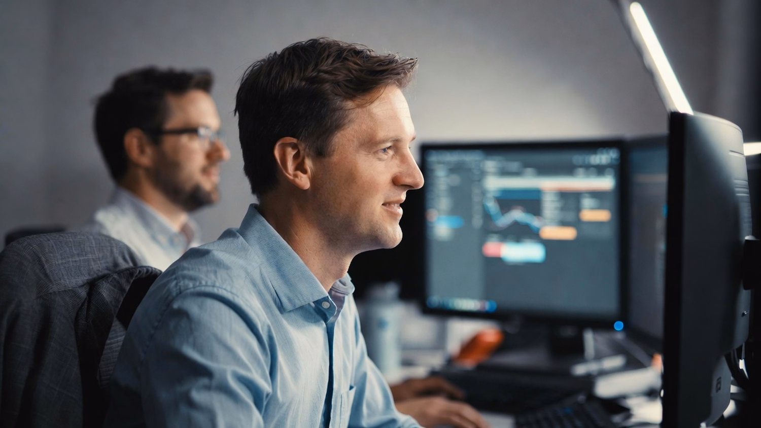 IT consultant focused on dual monitors, jacket on chair 65