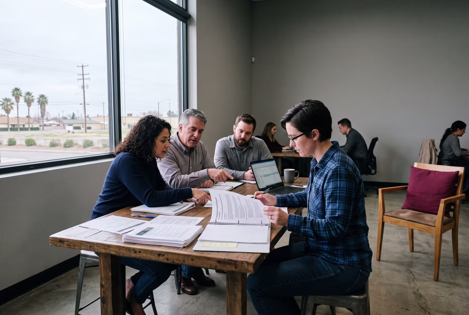 IT specialist reviewing proposal at coworking space with business owners, with Bakersfield landscape visible through window