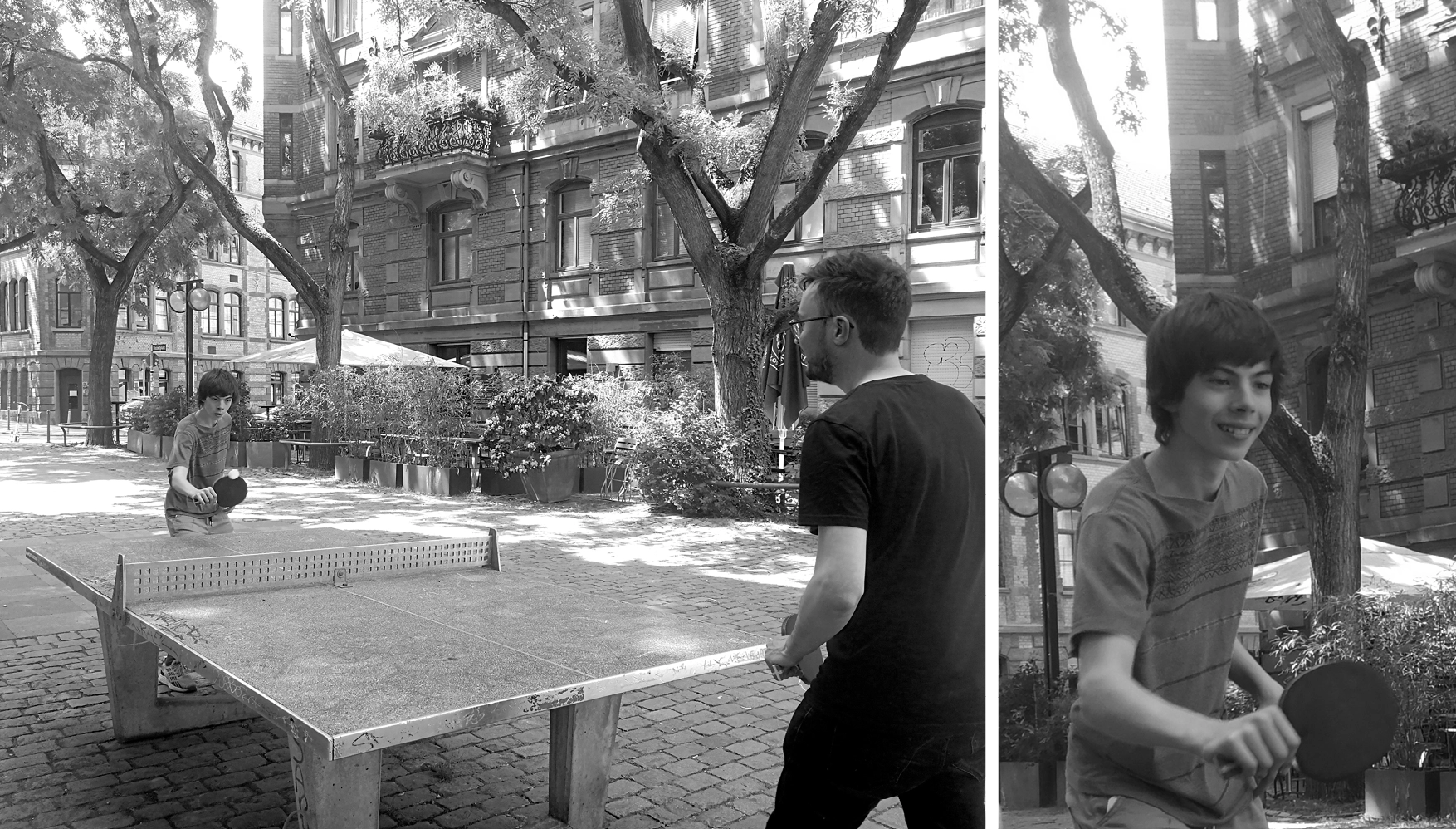 Two people playing table tennis outdoors on a stone-paved street surrounded by trees and old brick buildings.