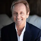 Smiling middle-aged man with light brown hair wearing a dark blazer and white shirt.