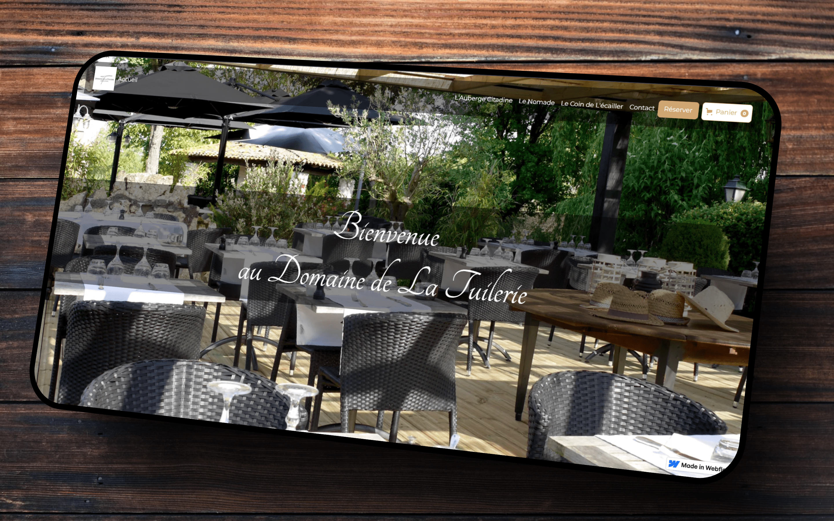 Un écran d'ordinateur affichant un site web de restaurant, "Le Domaine de la Tuilerie", présentant la page d'accueil , une photo de la terrasse de l'établissement sous la canisse