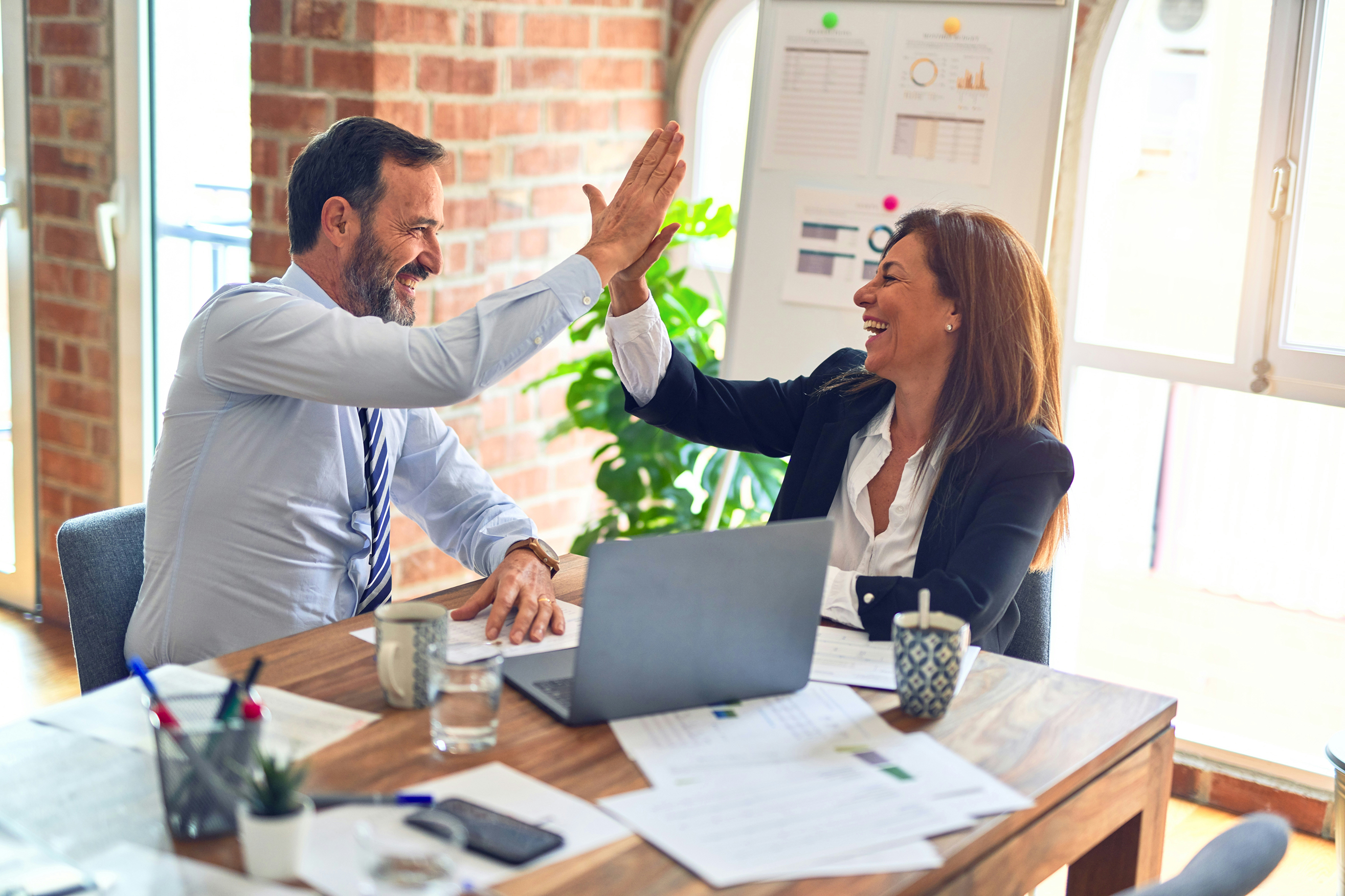 Affärspartners firar en lyckad fastighetsaffär och säkrad företagsfinansiering med en high-five på kontoret.