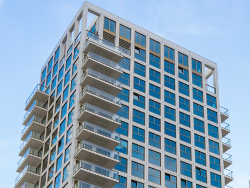 Modern hoog gebouw met glazen balkons onder een blauwe hemel.