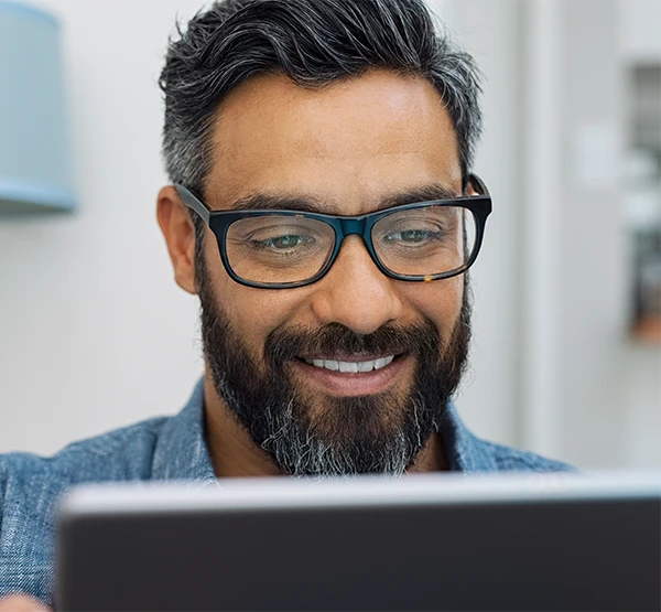 Smiling man with dark hair and beard wearing glasses looking at a tablet.
