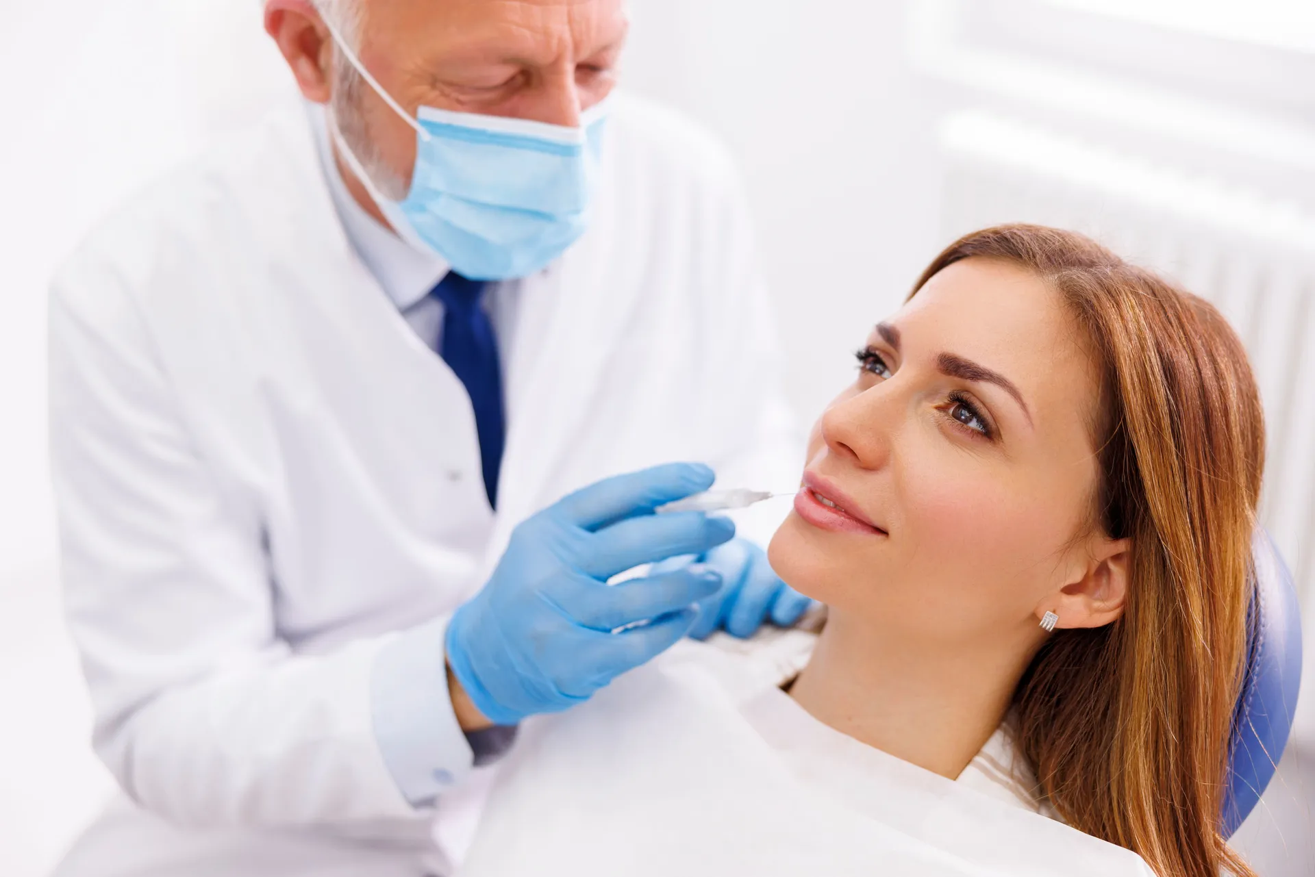 Woman receiving a lip injection from a doctor wearing blue gloves and a mask in a clinic.
