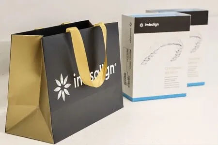 Invisalign branded shopping bag next to two Invisalign clear aligner boxes on a white surface.