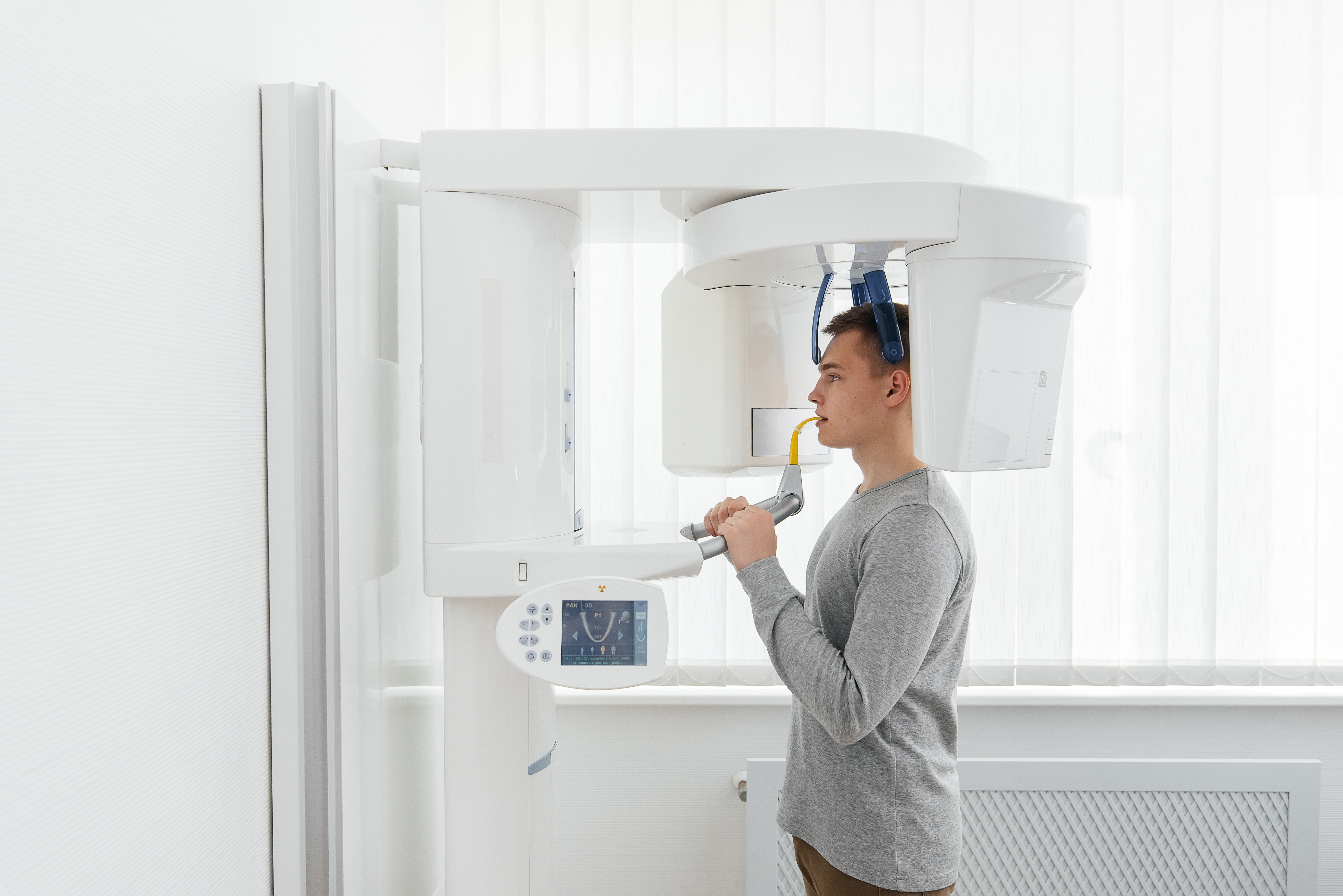 Young man undergoing a dental panoramic X-ray scan using a white digital dental imaging machine.