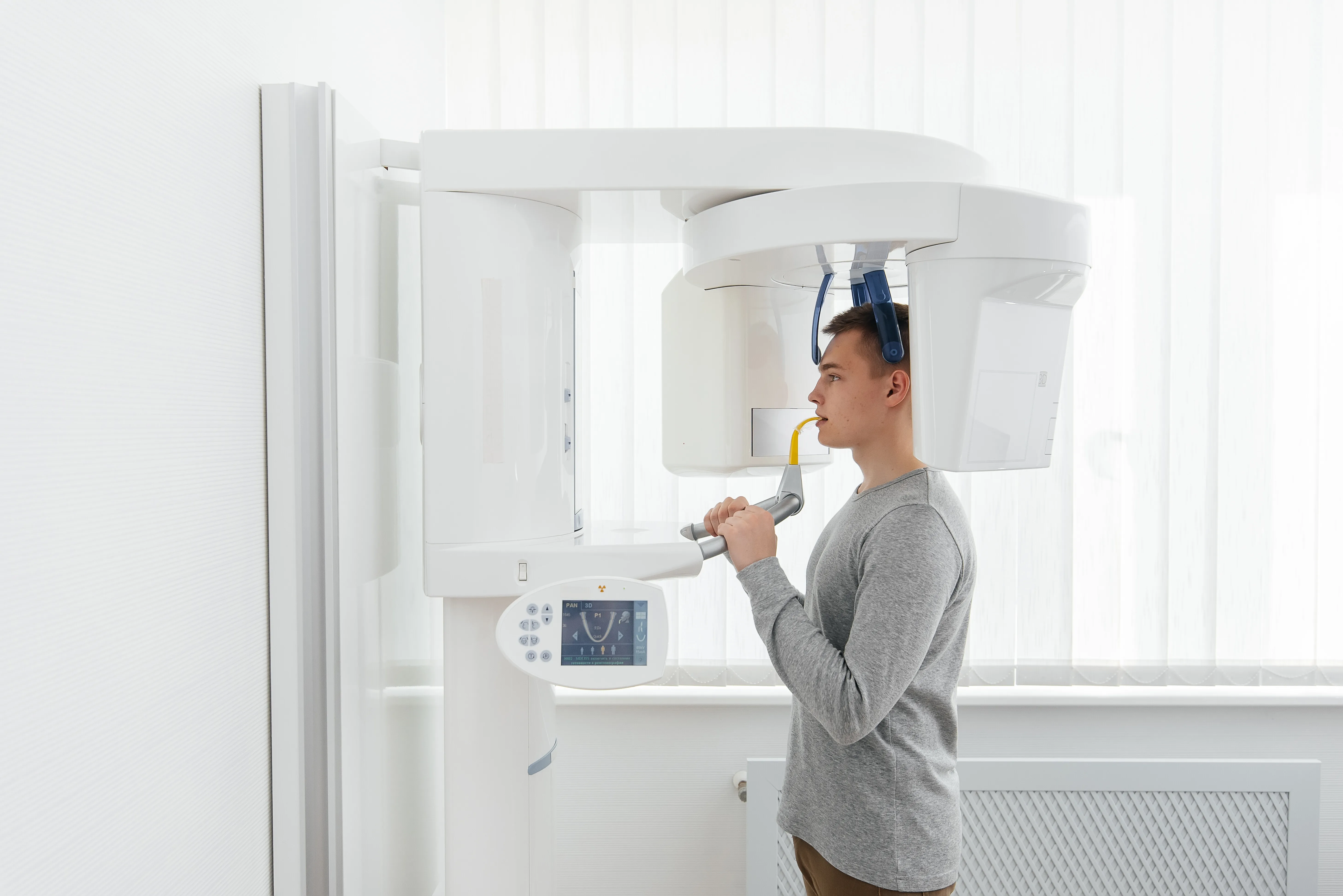 Young man undergoing a dental panoramic X-ray scan using a white digital dental imaging machine.