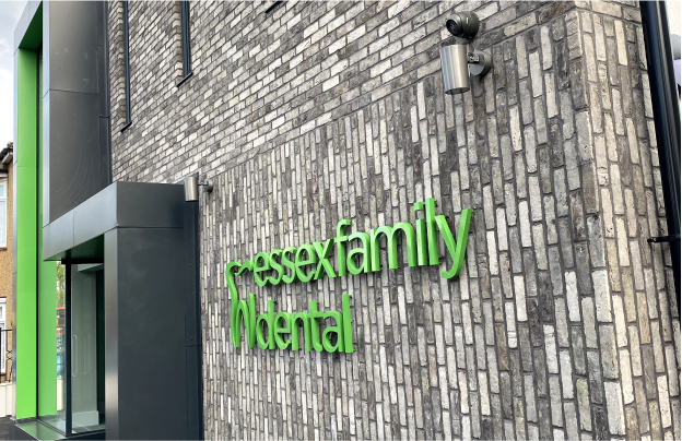 Exterior wall of a building with green 3D sign reading 'essexfamily dental' on a gray brick background.