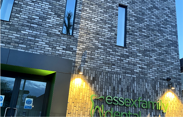 Exterior of a modern brick building at dusk with illuminated signs reading 'essexfamily dental'.