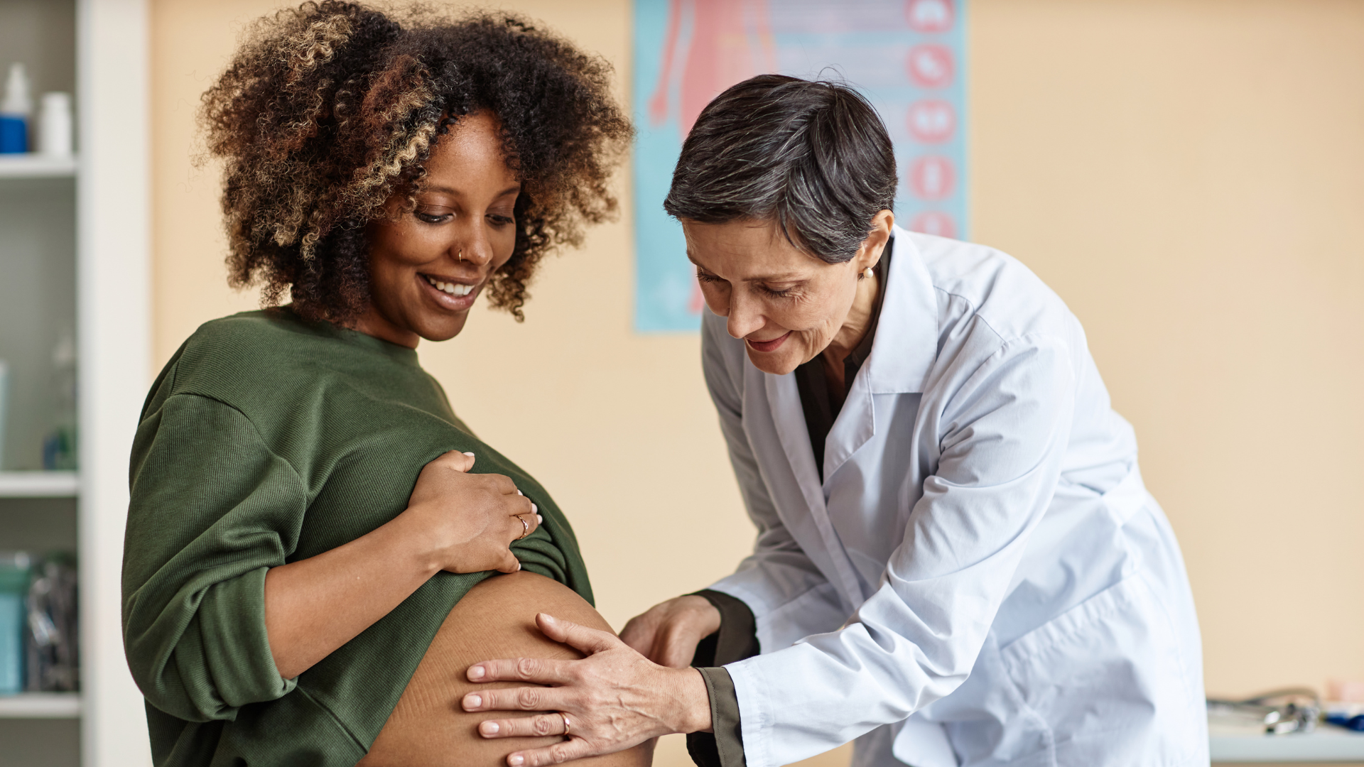 Pregnant woman smiling while a female doctor examines her belly in a medical office.
