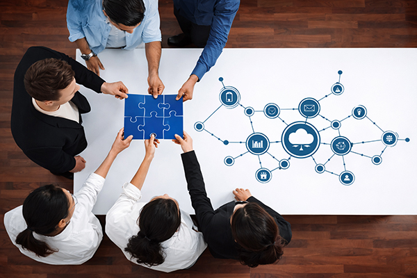 Groep van zes mensen die samen een blauwe puzzel in elkaar zetten boven een tafel met een infographic over netwerken.