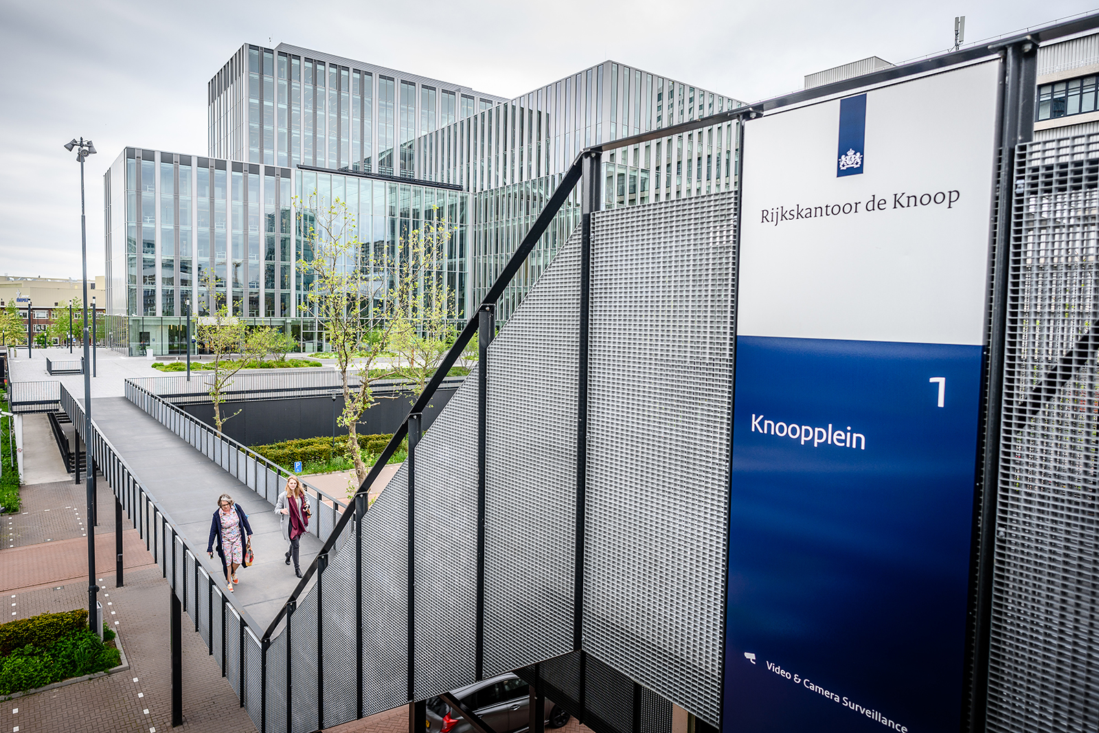 Moderne kantoorgebouwen met een loopbrug en een bord met de tekst 'Rijkskantoor de Knoop, Knooppelin 1'.