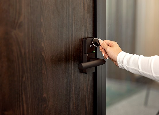 Hand houdt een slimme elektronische sleutel dicht bij een digitaal deurslot op een houten deur.