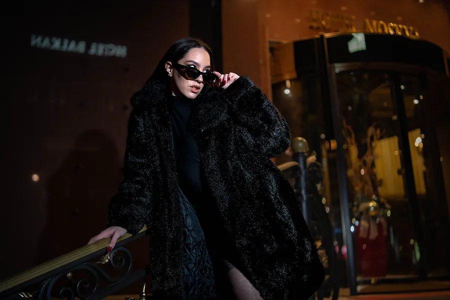 Modni portret žene u crnom kaputu ispred osvetljenog ulaza – noćna elegantna fotografija – Fotograf Mihajlo