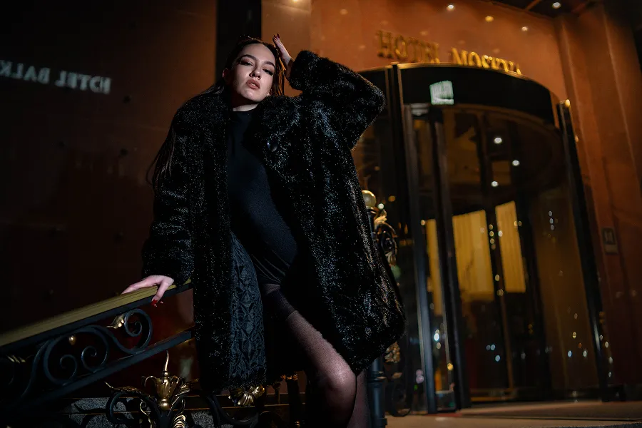 Modni portret mlade žene u tamnom kaputu ispred osvetljenog ulaza – noćna fotografija – Fotograf Mihajlo 
