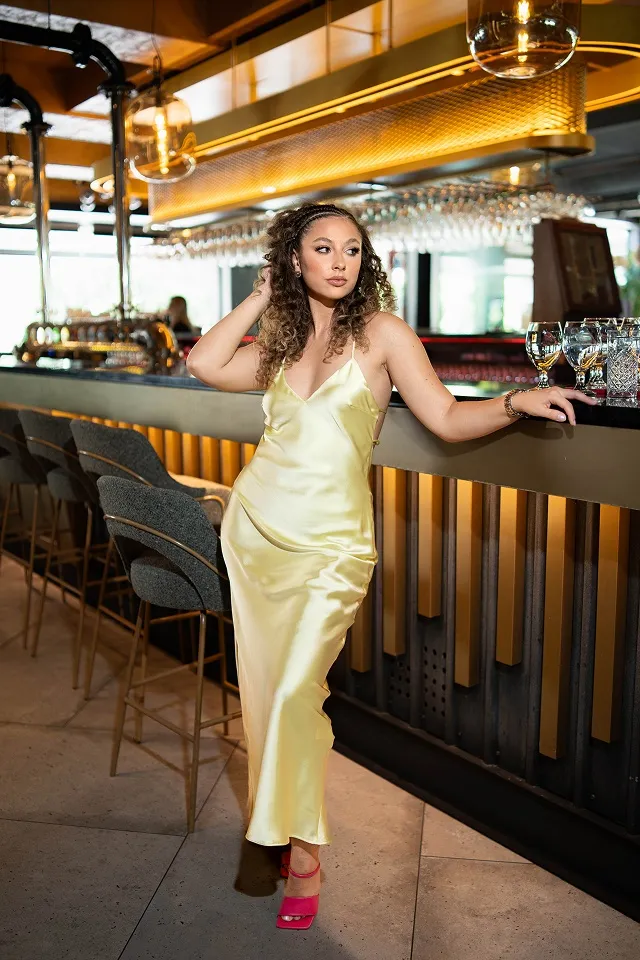 Portret devojke u satenskoj zlatnoj haljini koja pozira u modernom baru.