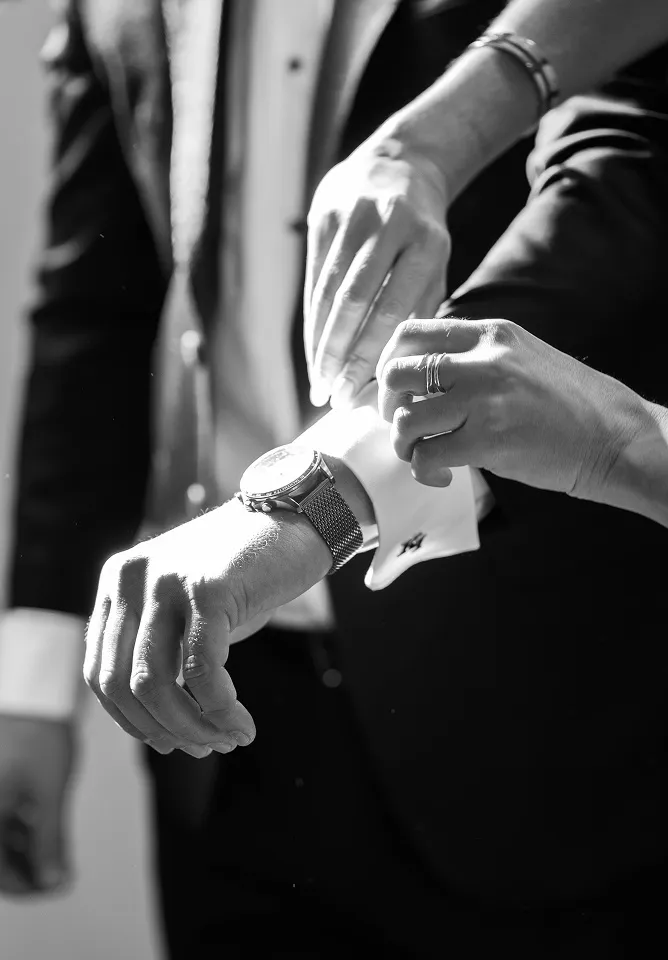 Mlada pomaže mladoženji da zakopča manžetnu, crno-bela fotografija.