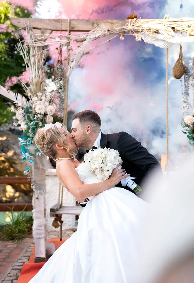 Romantičan poljubac mladenaca ispod floralne ceremonijalne dekoracije tokom venčanja u Nišu.