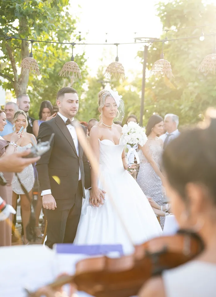 Svečani trenutak mladenaca tokom ceremonije uz sunčev sjaj i violinu u prvom planu.