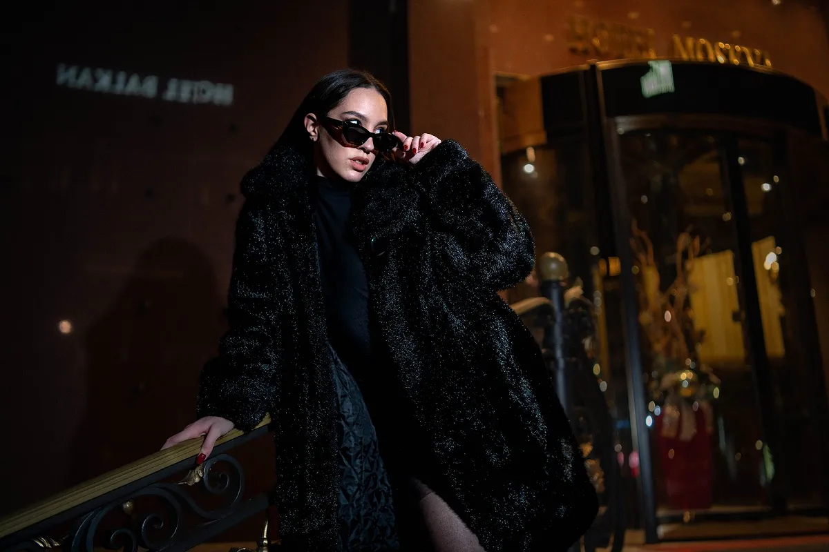 Modni portret devojke u crnom kaputu na ulazu u hotel Moskva u Beogradu, snimljen u večernjem ambijentu.