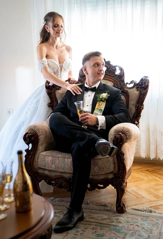 Mlada stoji iza mladoženje dok on sedi u dekorativnoj fotelji, portret mladenaca snimljen na venčanju u Nišu.