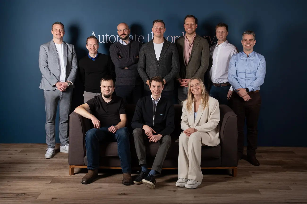 Group of ten professionals posed smiling in front of a blue wall with partial text, with three seated on a dark sofa and seven standing behind.
