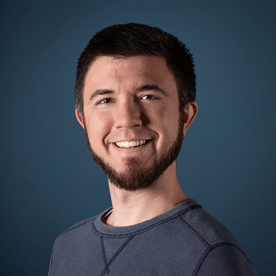 Smiling person with short blond hair and hoop earrings wearing a textured jacket.