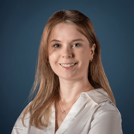 Smiling young woman with long blonde hair wearing a black top with white embroidery.