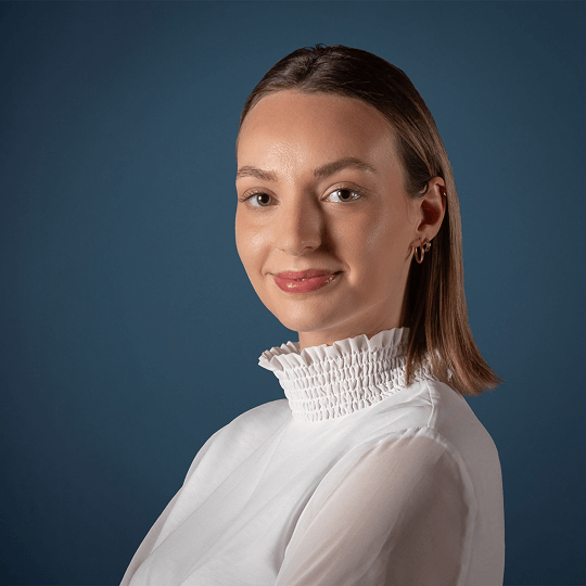 Smiling woman with shoulder-length blonde hair wearing a white top with a ruffled collar.