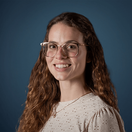 Smiling woman with curly hair and glasses wearing a black shirt.