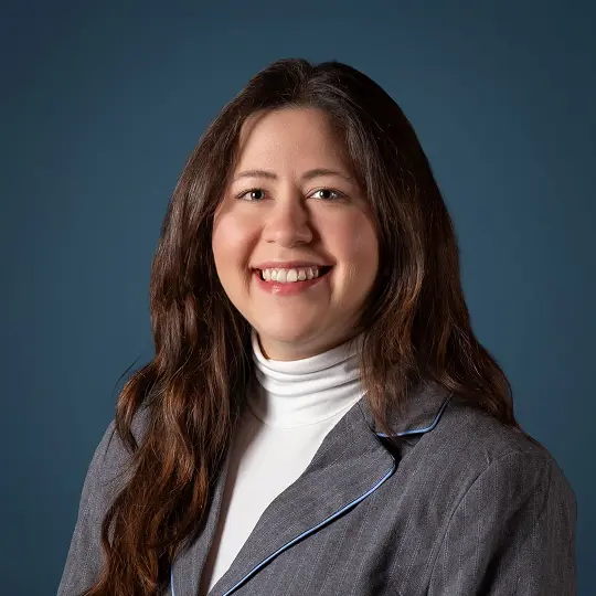 Smiling woman with long brown hair wearing a white blouse against a white background.