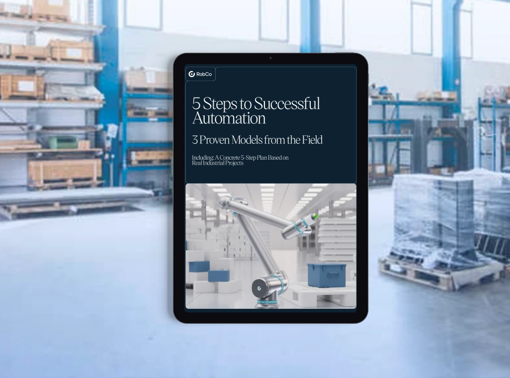 A tablet displays the cover of a RobCo whitepaper titled "5 Steps to Successful Automation." Subtitle: "3 Real-World Success Models." The cover features a modular robotic arm moving boxes in an industrial setting. In the background, a warehouse with shelves, cardboard boxes, and pallets is visible.