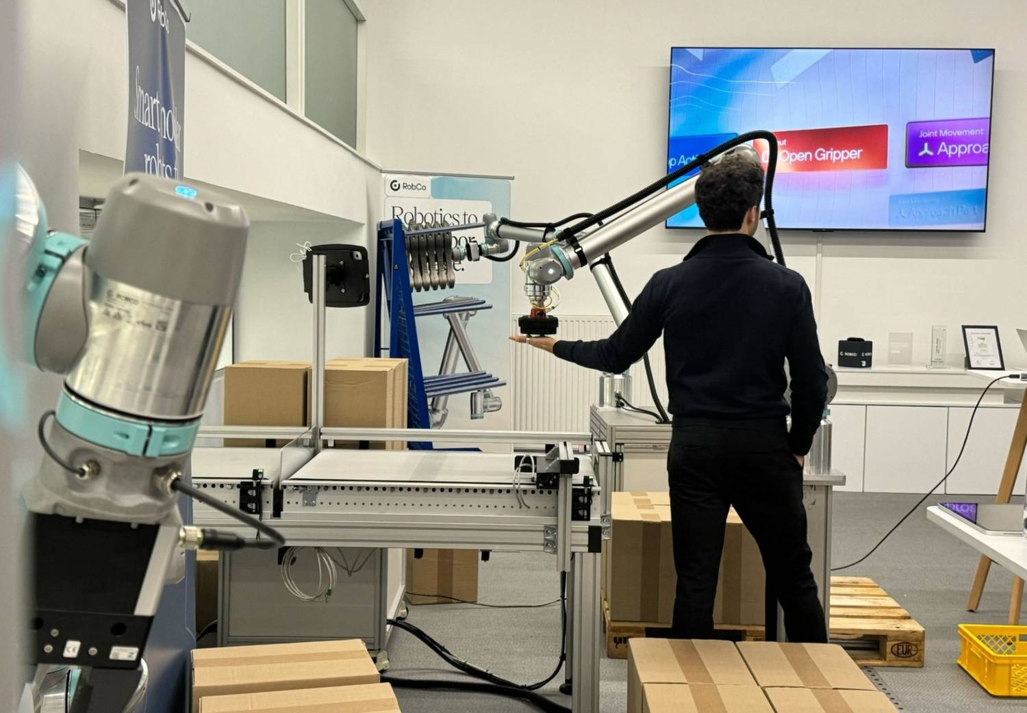 Ein Mitarbeiter arbeitet Hand in Hand mit einem Roboter, der ihm ein Bauteil anreicht, und demonstriert so, wie Unternehmen mit kollaborativer Robotik sicher automatisieren können.