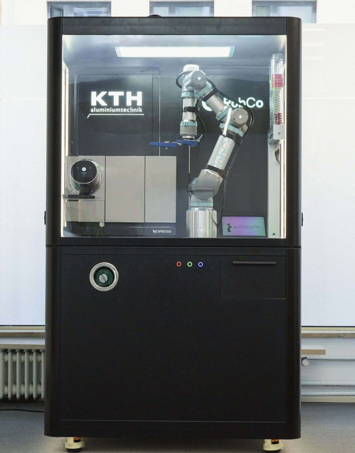 Ein Roboterarm von RobCo bedient eine Kaffeemaschine in einer gläsernen Zelle und demonstriert als Show-Case die Zukunft der Fertigung und serviceorientierter Automation.