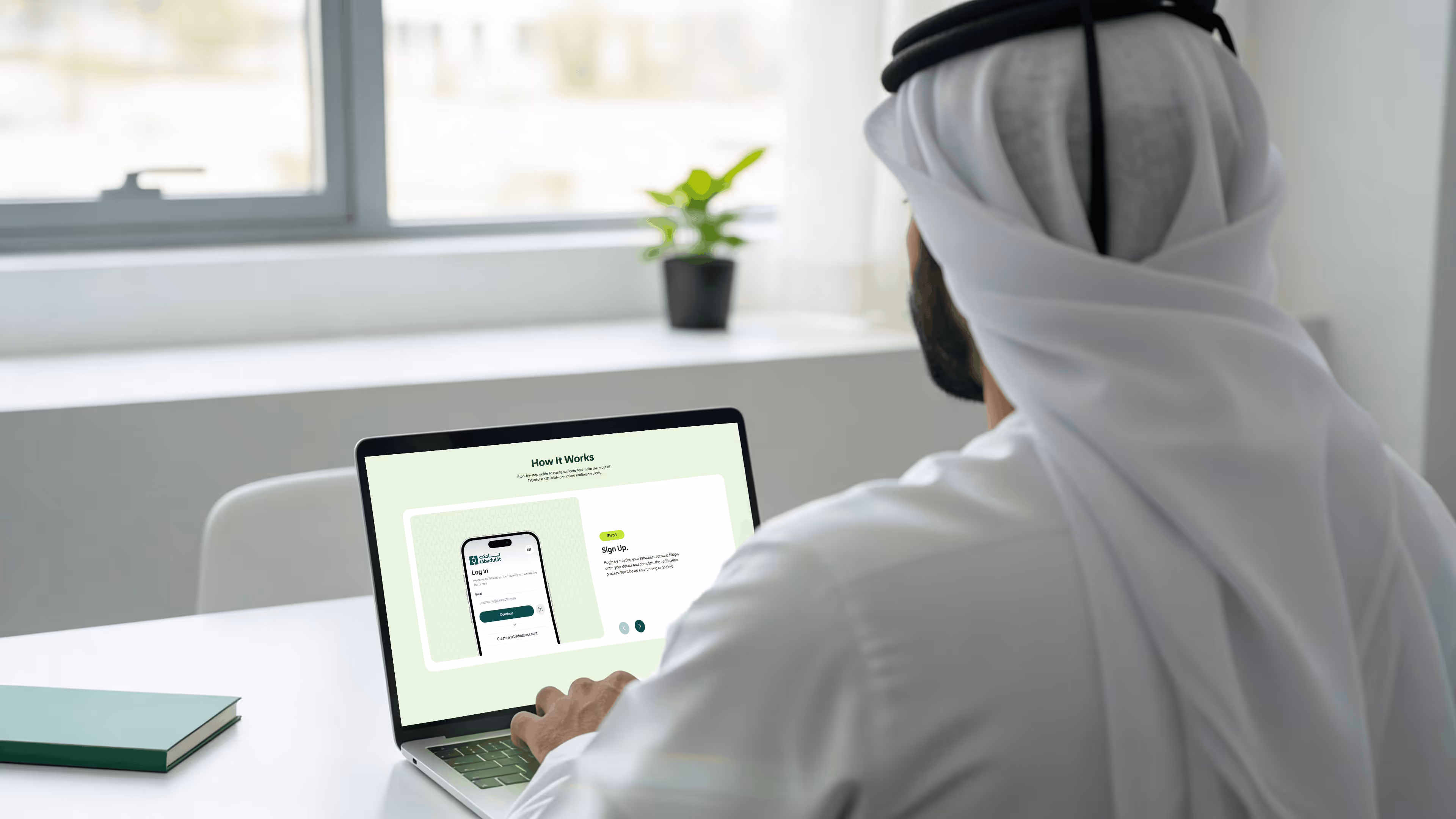 Man in traditional Gulf attire using a laptop with a financial web platform open in a modern office.