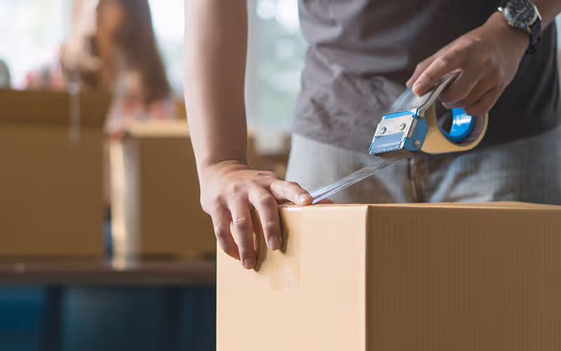 Person verschließt einen Karton mit Verpackungsklebeband.