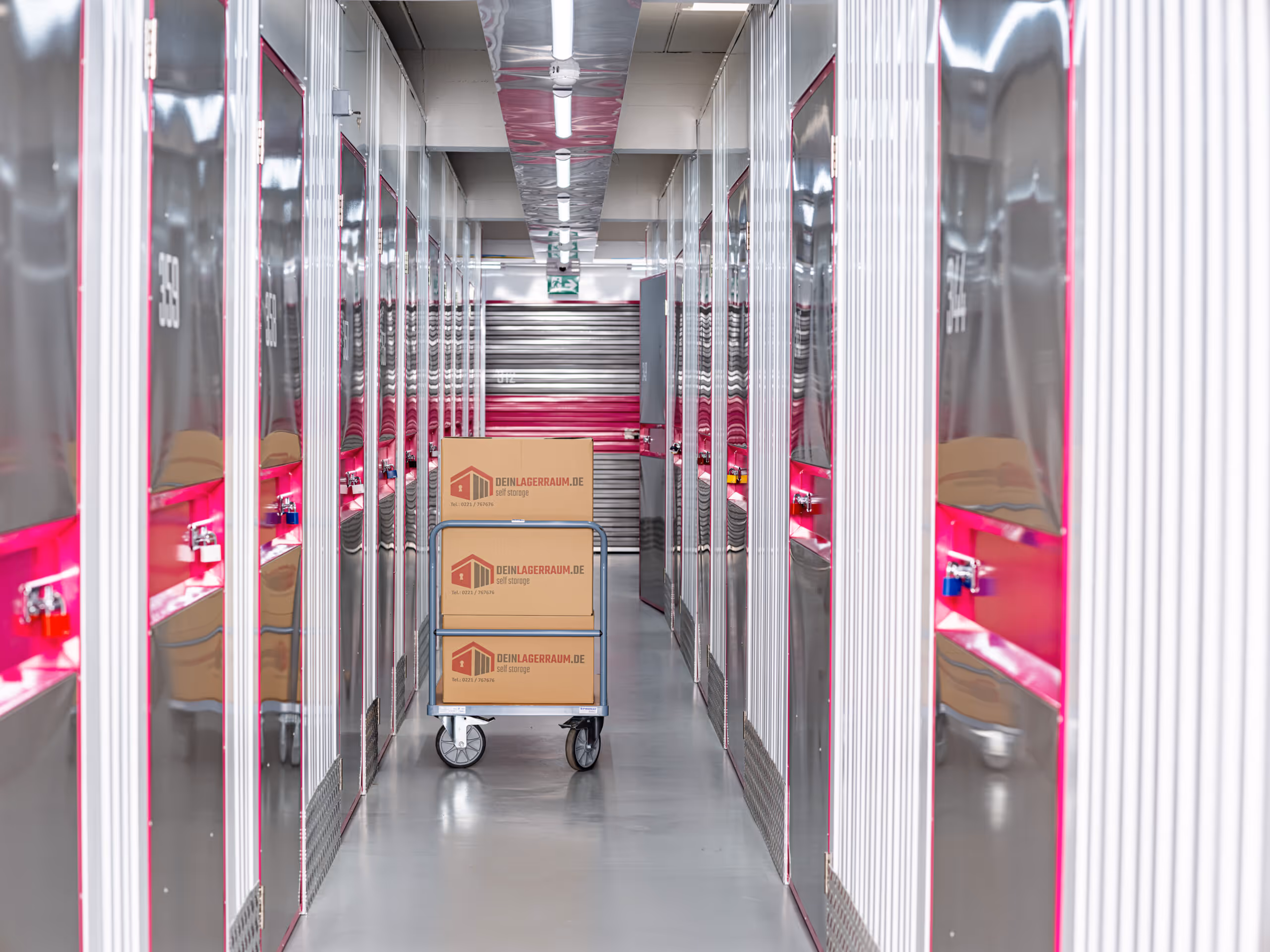Korridor mit Metalllagerschränken auf beiden Seiten und einem Wagen mit Kartons in einem Selfstorage-Lager.