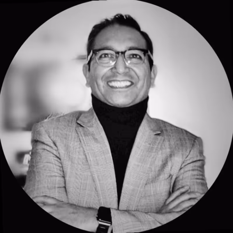 Smiling man wearing glasses and a checked blazer over a black turtleneck with arms crossed.