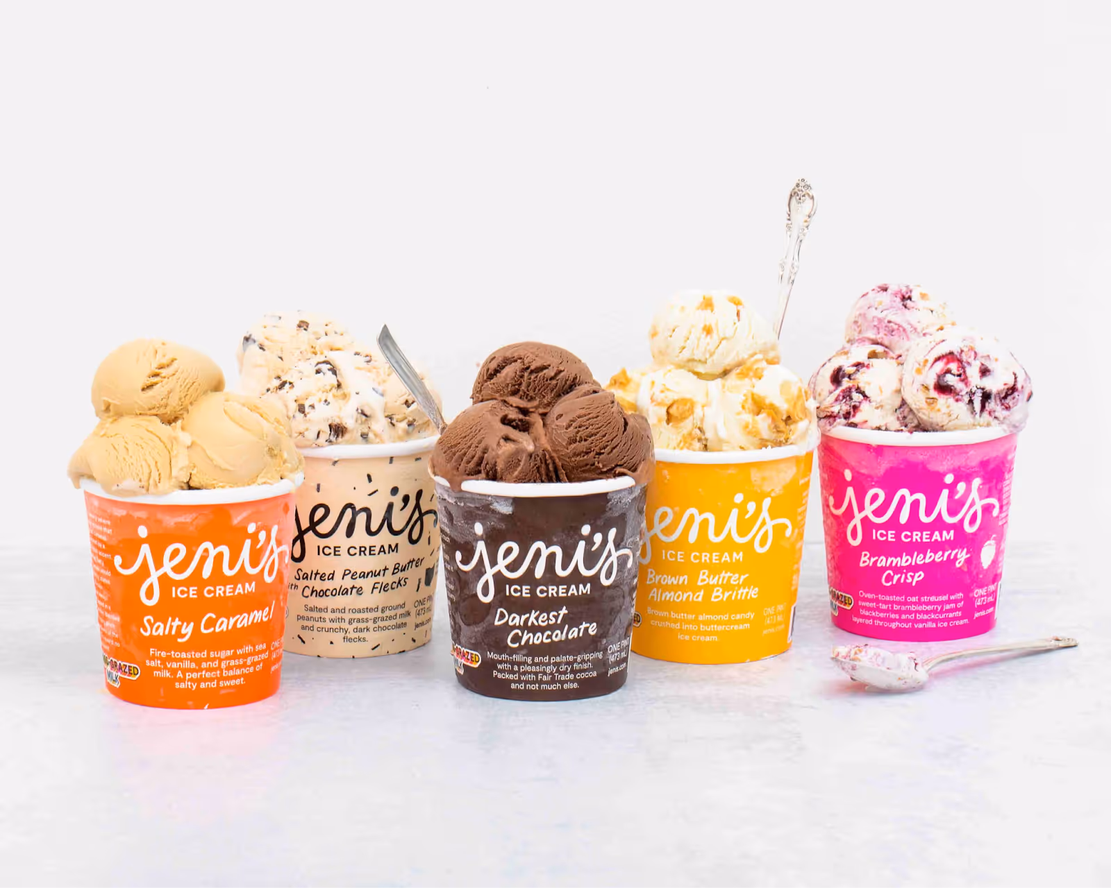 Five colorful Jeni's ice cream cups with scoops of various flavors including Salty Caramel, Salted Peanut Butter with Chocolate Flecks, Darkest Chocolate, Brown Butter Almond Brittle, and Brambleberry Crisp.