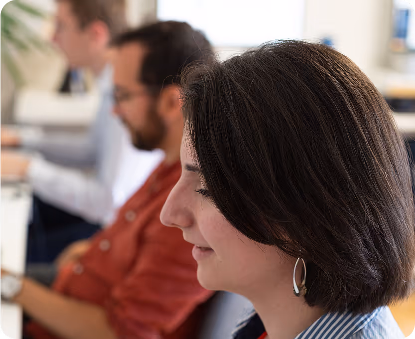 Une chercheuse en premier plan souriant légèrement et en fond flouté deux autres chercheurs en train de travailler