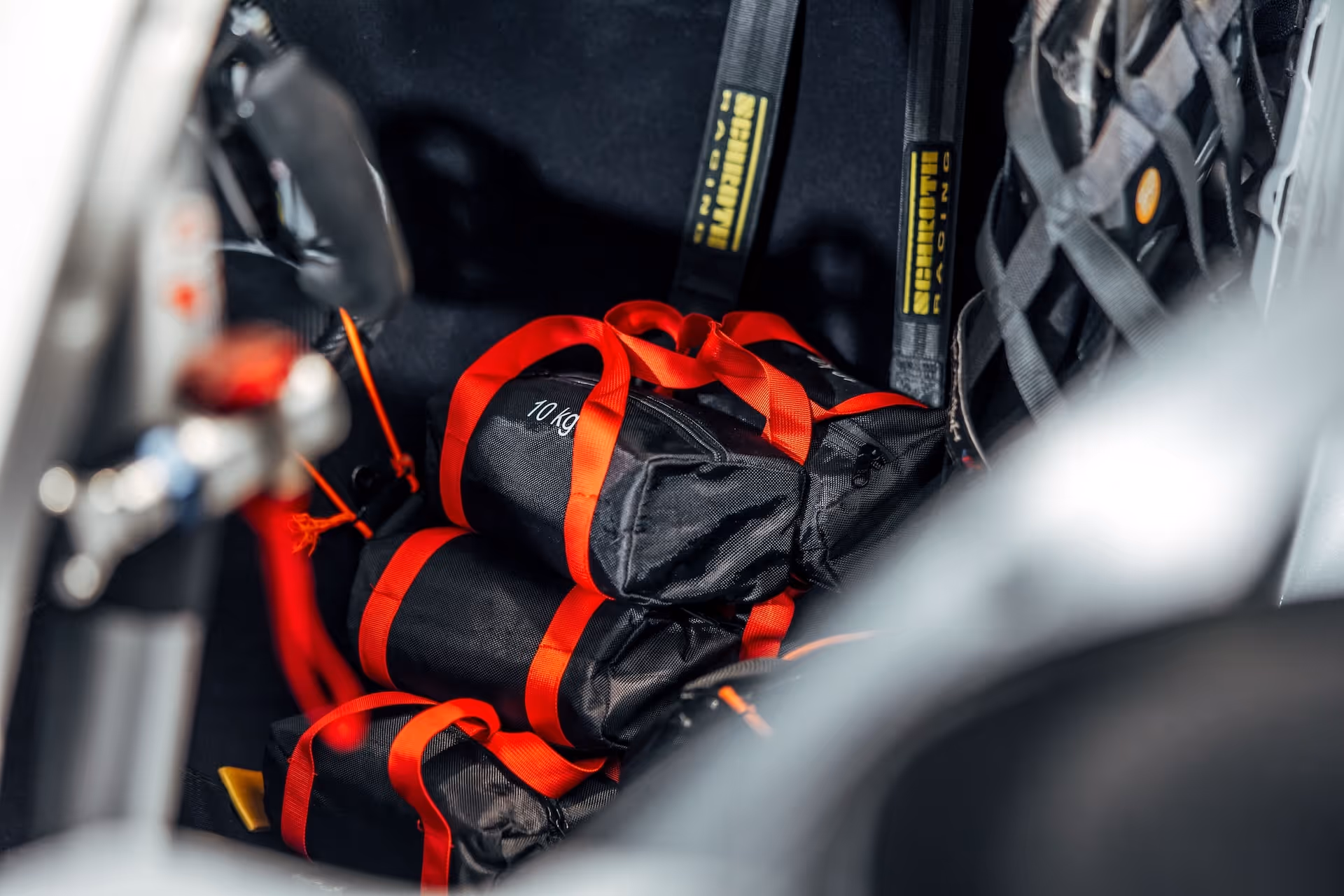 Stack of black and red 10 kg weighted bags inside a vehicle compartment with harness straps.