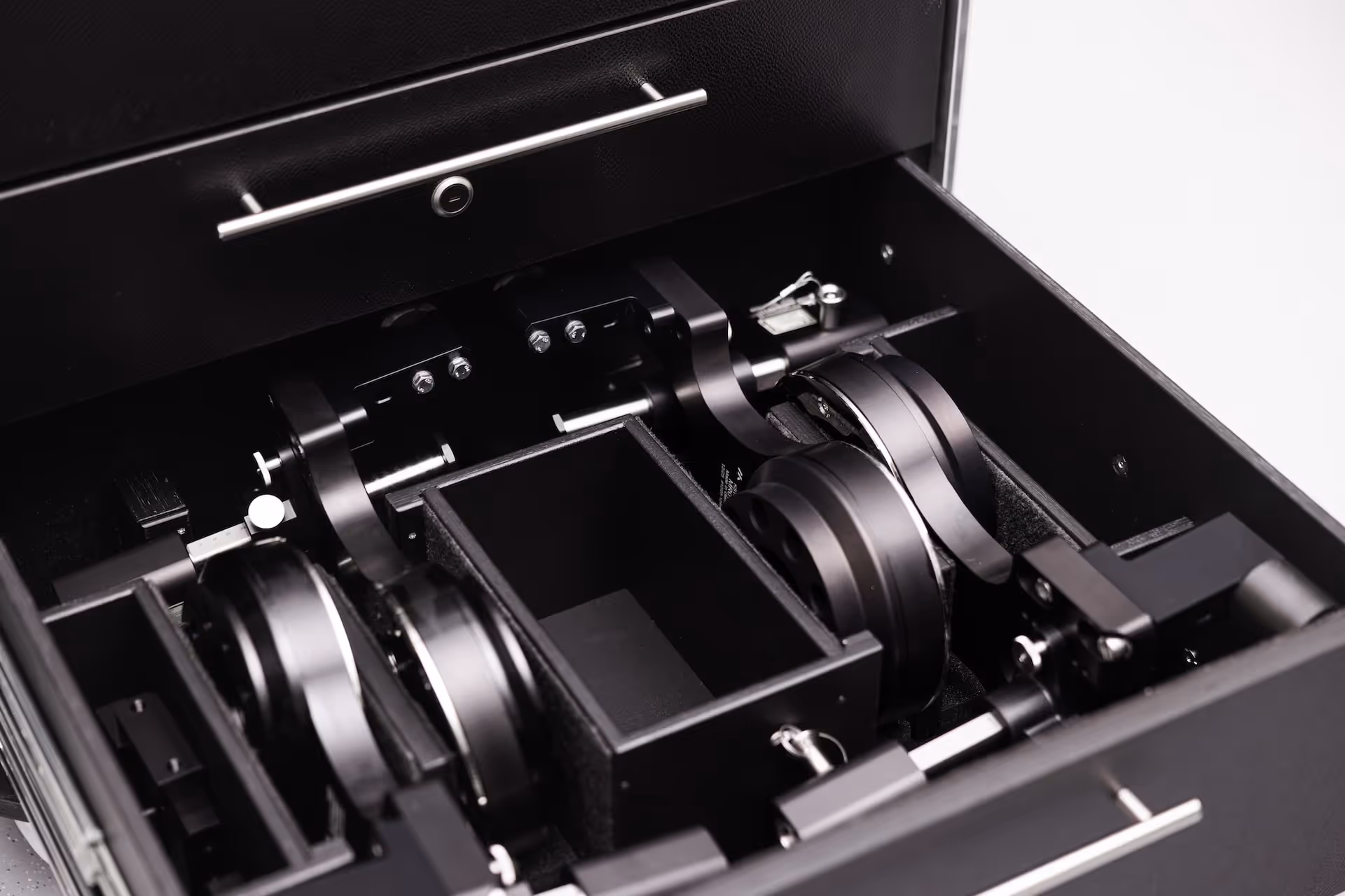 Open black drawer containing mechanical and electronic components including two large circular metallic parts and a pair of keys.