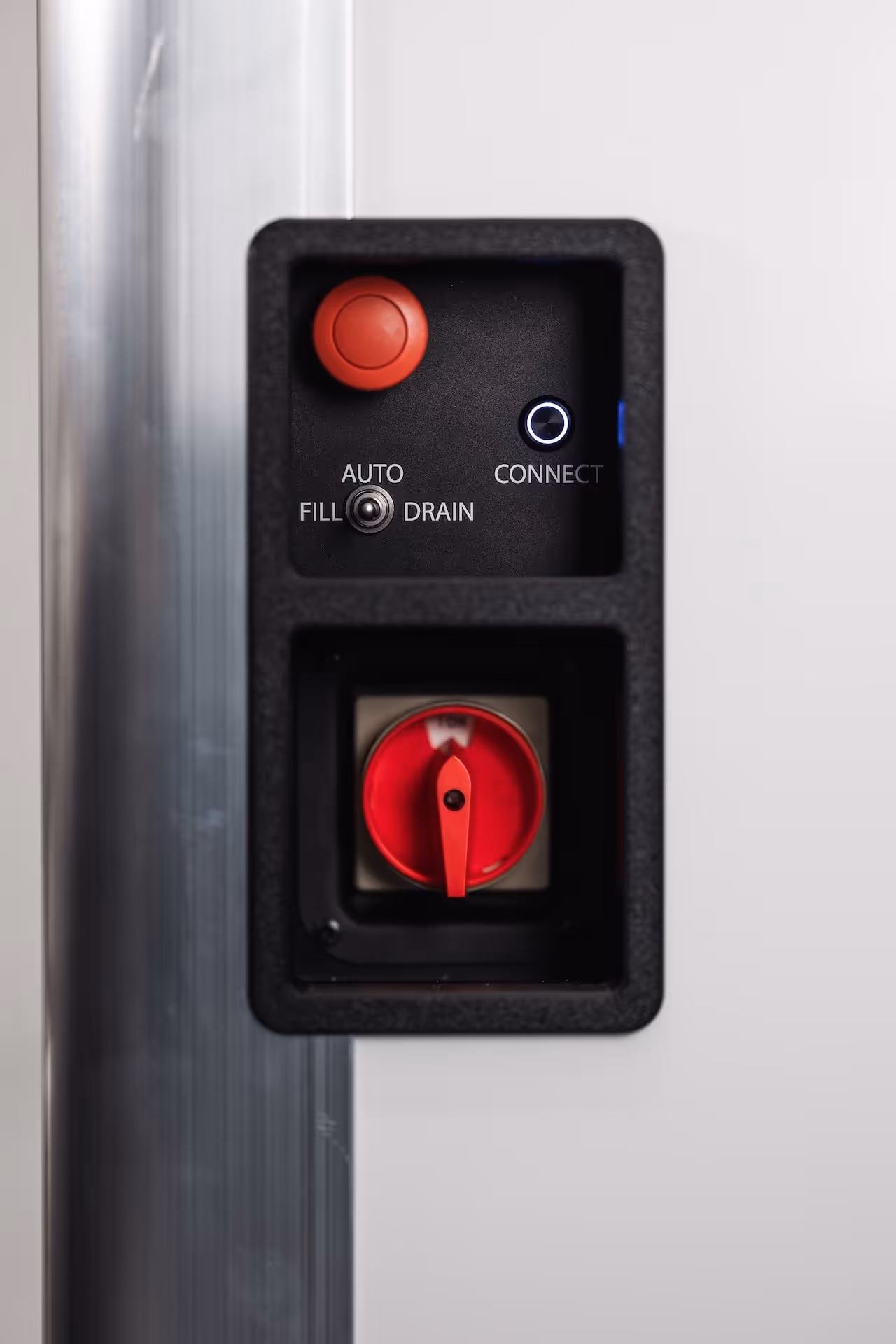 Close-up of a control panel with a red emergency stop button, a toggle switch labeled AUTO, FILL, DRAIN, and a red rotary switch.