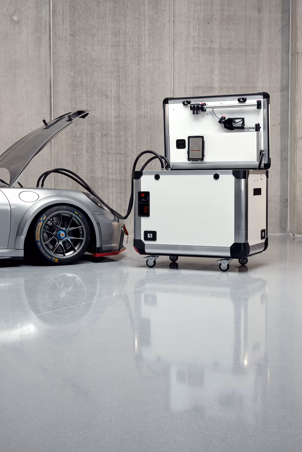 Silver sports car connected to a white portable fuel container with open lid on a polished concrete floor.