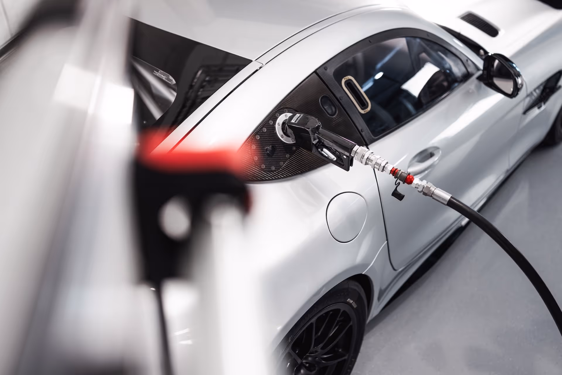 Silver racecar refueling with a fuel nozzle attached to a black carbon fiber fueling port.